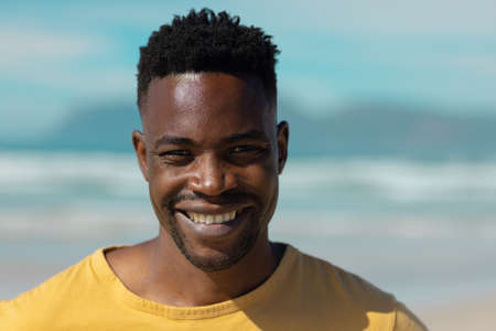 Close-up portrait of smiling african american young man against sea and sky on sunny day. nature,...
