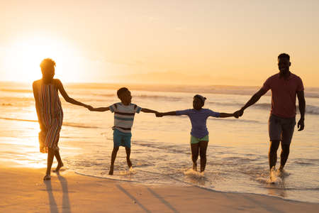 African american young parents holding son and daughter&#39;s hands while standing at shore against sky. nature, copy space, unaltered, beach, childhood, family, togetherness, enjoyment and holiday.の写真素材