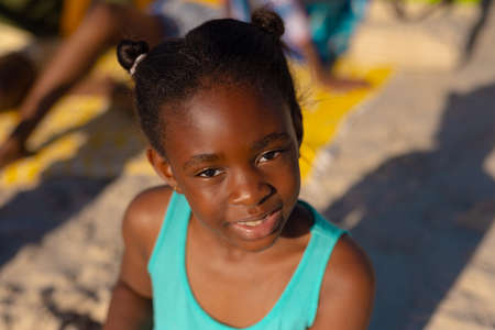 High angle portrait of african american cute girl sitting at beach during sunny day. childhood, summer, unaltered, beach, lifestyle, enjoyment and holiday concept.の写真素材