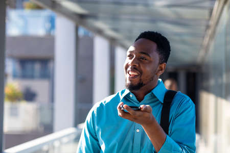 Happy african american businessman talking through smartphone speaker at corridor. unaltered, technology, occupation and business concept.の写真素材