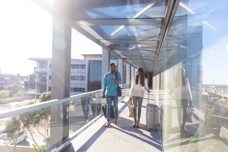 Full length of young biracial businessman and businesswoman with luggage walking at airport corridor. unaltered, occupation, business travel and transportation concept.の写真素材
