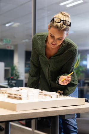 Caucasian female architect analyzing model on desk with pencil at modern workplace. unaltered, creative business and modern office concept.の写真素材