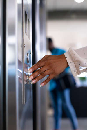 Hand of young biracial businesswoman pressing elevator button at modern workplace. unaltered, business, modern office, convenience and technology concept.の写真素材