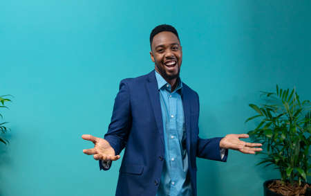 Portrait of happy african american businessman gesturing while standing against blue wall....