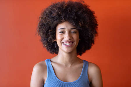 Portrait of beautiful happy hispanic businesswoman with afro hairstyle against brown background....
