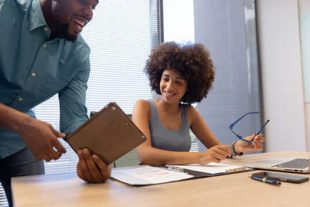 Happy biracial business colleagues discussing over digital tablet in modern workplace. unaltered,...