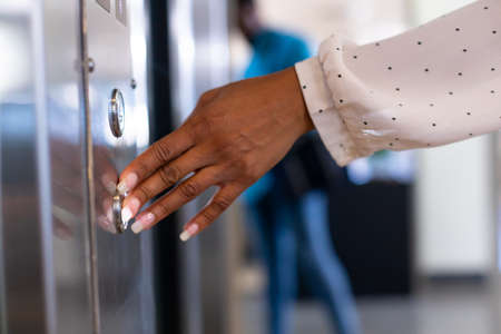 Cropped hand of young biracial businesswoman pressing elevator button at modern workplace. unaltered, business, modern office, convenience and technology concept.の写真素材