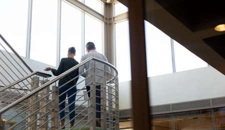 Low angle view of caucasian colleagues discussing while moving up on staircase at modern workplace....