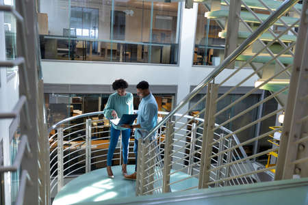 High angle view of african american professionals discussing over file at staircase in workplace....