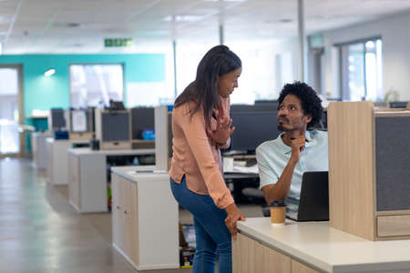 Confident biracial male and female colleagues discussing together in cubicle at modern workplace....