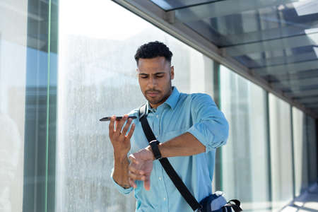 African american businessman checking time while talking on smartphone through speaker in corridor....