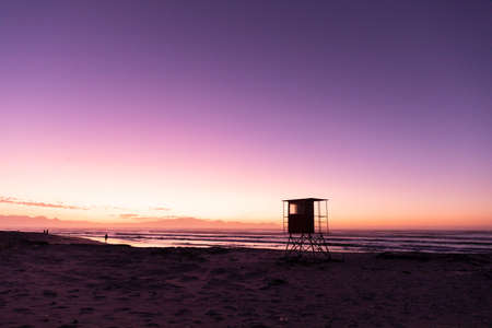 View of silhouette lifeguard hut on sandy beach against sea and clear purple sky, copy space. unaltered, nature and protection concept.の写真素材