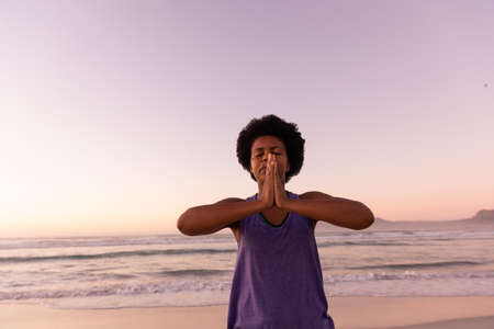 African american mature woman with afro hair meditating in prayer pose at beach against clear sky....