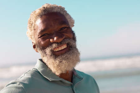 Close-up portrait of cheerful bearded african american senior man against sea and blue sky in...