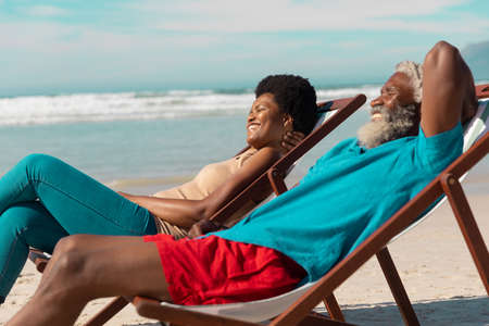 Happy african american couple relaxing on deckchairs against sea and cloudy sky on sunny day. nature, unaltered, love, togetherness, retirement, enjoyment and holiday concept.の写真素材