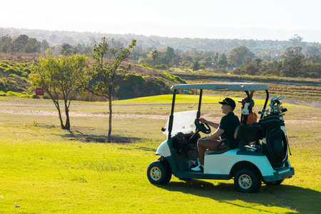 Multiracial young male friends riding in golf cart against clear sky at golf course in summer. copy space, transportation, unaltered, friendship, togetherness, nature, sport and weekend activities.の写真素材