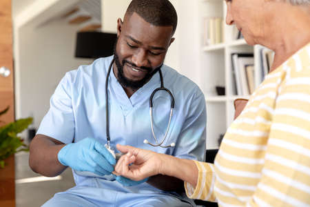 African american male health worker measuring blood sugar of caucasian senior woman using...