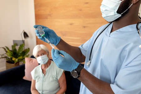 Mid section of african american male health worker filling the syringe from vail bottle at home. Medical care and retirement senior lifestyle conceptの写真素材