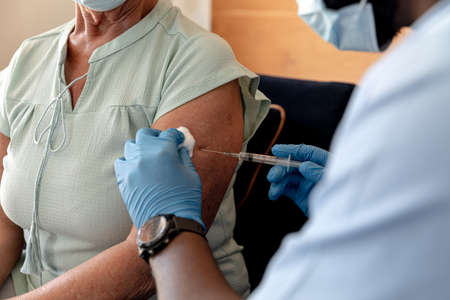 Mid section of african american male health worker giving an injection to caucasian senior woman. Medical care and retirement senior lifestyle conceptの写真素材