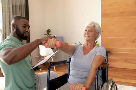 African american male physiotherapist helping caucasian senior woman to do exercise with dumbbells....