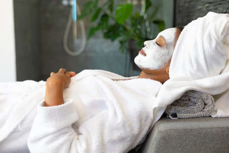 African american woman in a bathrobe with facial beauty mask relaxing at home. Spa, wellness and relaxation conceptの写真素材