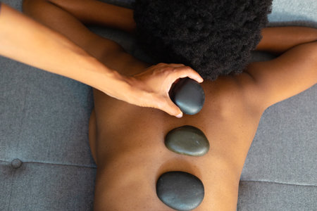 African american woman woman receiving hot stone massage at home. Spa, wellness and relaxation conceptの写真素材