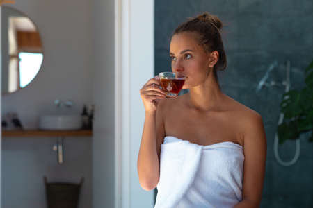 Caucasian young woman in a bathrobe drinking tea at home. Self-care, hygiene and relaxation concept