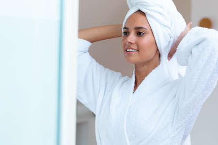 Caucasian woman in a bathrobe looking in the mirror at home. Self-care, hygiene and relaxation conceptの写真素材