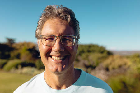 Close-up portrait of smiling caucasian senior man wearing eyeglasses against clear blue sky in yard....