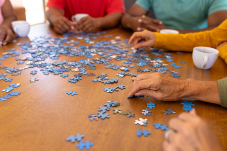 Cropped hands of multiracial seniors arranging jigsaw pieces on wooden table in nursing home. Puzzle, game, confusion, brainstorming, unaltered, togetherness, support, assisted living, retirement.の写真素材