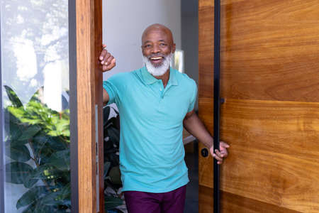 Portrait of cheerful african american senior man welcoming while standing at doorway in nursing...