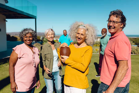 Portrait of happy multiracial senior friends playing rugby in yard against clear sky at nursing home. Summer, unaltered, sport, togetherness, enjoyment, support, assisted living, retirement concept.の写真素材
