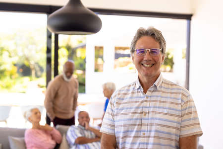 Portrait of smiling caucasian senior man standing with multiracial friends in background. Nursing...