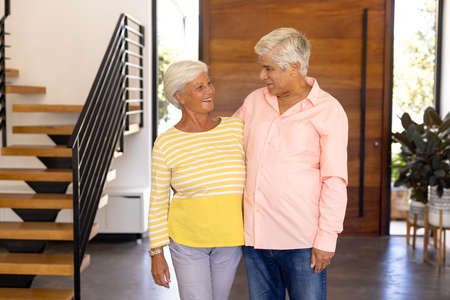 Smiling biracial senior friends looking at each other while standing against door in nursing home. Happy, unaltered, friendship, togetherness, support, assisted living and retirement concept.の写真素材