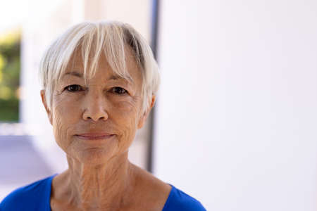 Close-up portrait of smiling asian senior woman with short hair against white wall in nursing home....