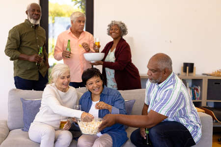 Multiracial senior friends enjoying beer and popcorn while watching soccer match in nursing home. Sport, happy, food, alcohol, unaltered, togetherness, support, assisted living and retirement.の写真素材