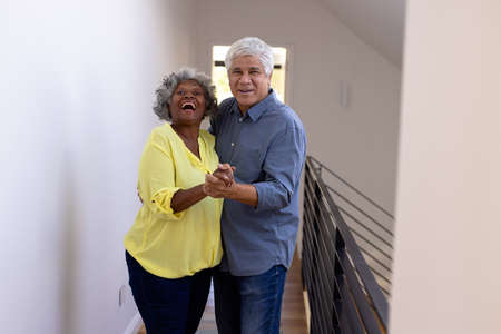 Portrait of cheerful multiracial senior friends dancing by wall in corridor at nursing home. Copy...