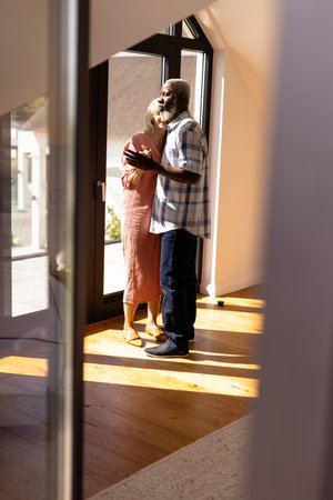 Multiracial senior friends dancing by window on hardwood floor in nursing home, copy space. Sunlight, togetherness, enjoyment, unaltered, recreation, support, assisted living and retirement concept.の写真素材