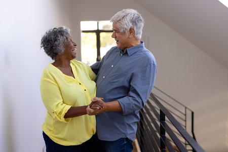 Cheerful multiracial senior friends looking at each other while dancing in corridor at nursing home. Copy space, togetherness, enjoyment, unaltered, recreation, support, assisted living, retirement.の写真素材