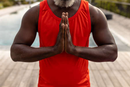 Midsection of african american senior man meditating in prayer position while standing in yard. Yoga, zen, unaltered, support, assisted living, retirement home, fitness and active lifestyle concept.の写真素材