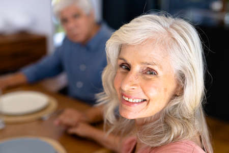 Close-up portrait of smiling caucasian senior woman holding biracial man's hand at dining table....