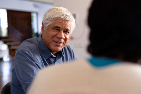 Smiling biracial senior man talking with female friend while sitting for lunch in nursing home....