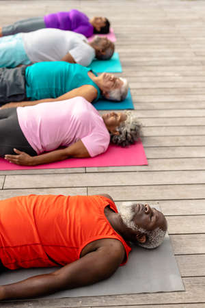 Multiracial senior friends with eyes closed exercising while lying on mats over hardwood floor....