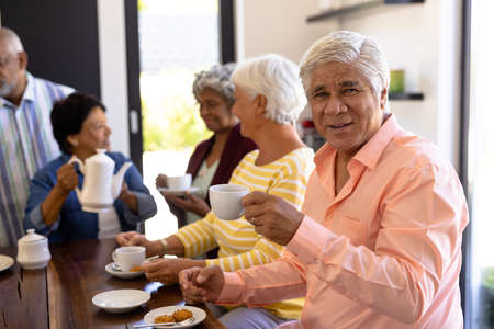 Portrait of biracial senior man having coffee and cookies with multiracial friends at table. Snacks, drink, food, unaltered, friendship, togetherness, support, assisted living and retirement home.の写真素材