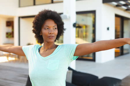 Confident young afro african american woman with arms outstretched exercising in backyard....