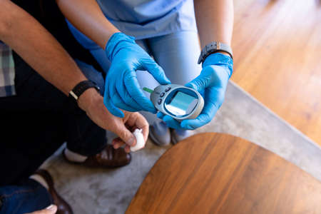 Mid section of biracial female health worker measuring blood sugar of senior man using glucometer....
