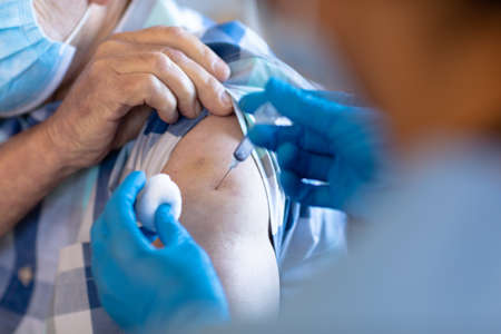 Biracial female health worker giving an injection to caucasian senior man at home. Medical care and...