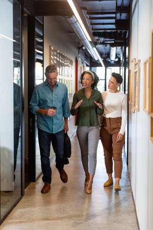 Multiracial businessman and businesswomen discussing while walking in corridor of office building....