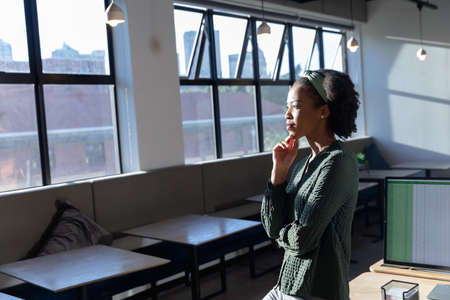 Thoughtful african american young businesswoman with hand on chin in office. Unaltered, creative business, workplace, occupation, contemplation.の写真素材