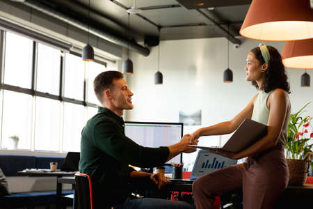 Multiracial young businessman and businesswoman handshaking in creative office. Unaltered, creative...